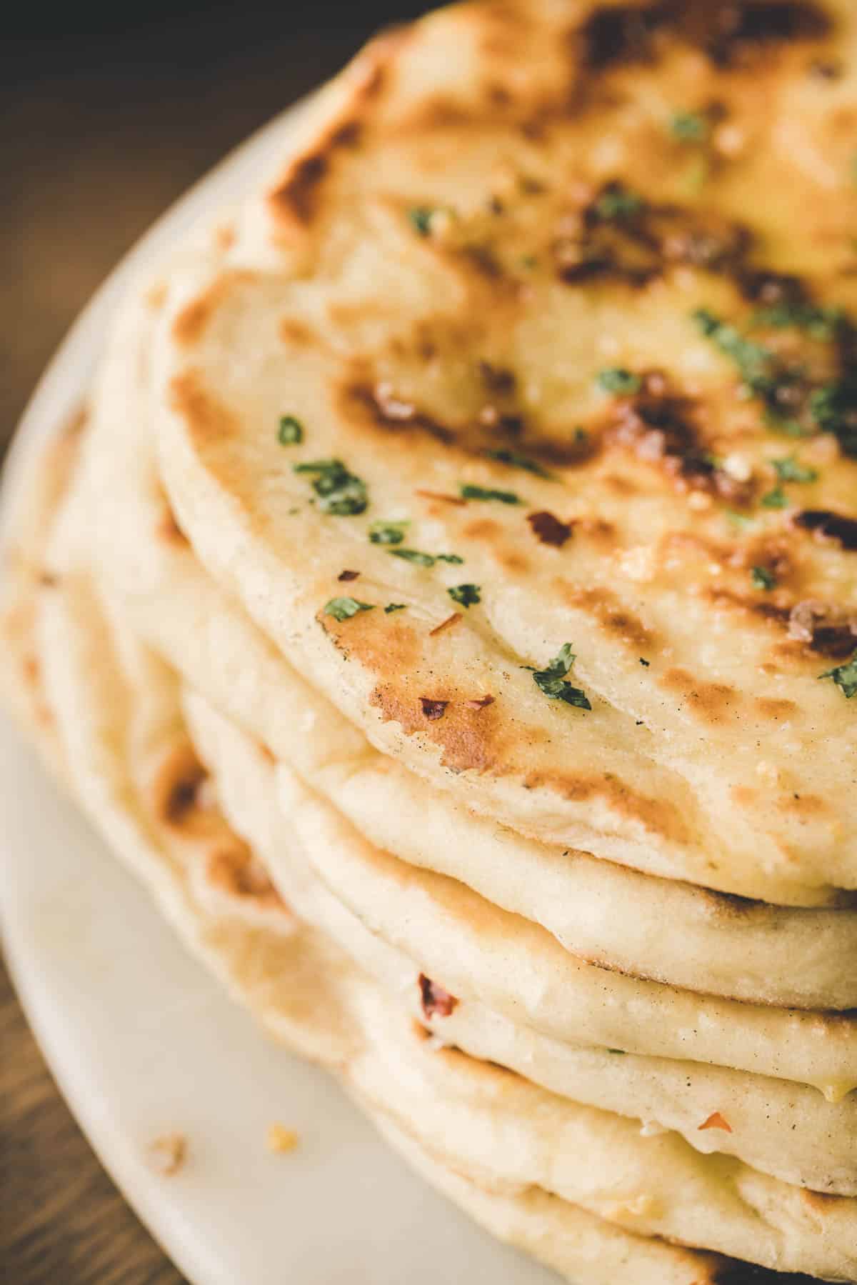 A close-up of a stack of naan bread topped with chopped herbs on a white plate.