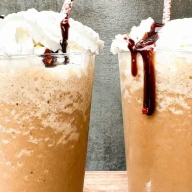 Two iced coffee drinks topped with whipped cream and chocolate syrup, each served in a clear glass with a straw—perfect for anyone seeking inspiring coffee ideas and bold coffee flavors.