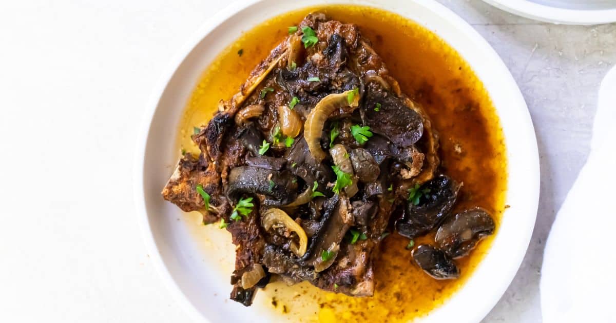 A plate of flavorful braised meat topped with cooked onions, mushrooms, and fresh herbs in a brown sauce—perfect for those seeking low carb or Keto recipes.