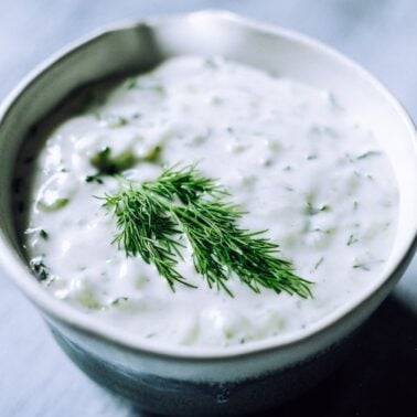 A bowl of creamy white, gluten-free dip garnished with fresh dill on top, set on a light-colored surfaceโa perfect addition to your collection of gluten-free sauces.