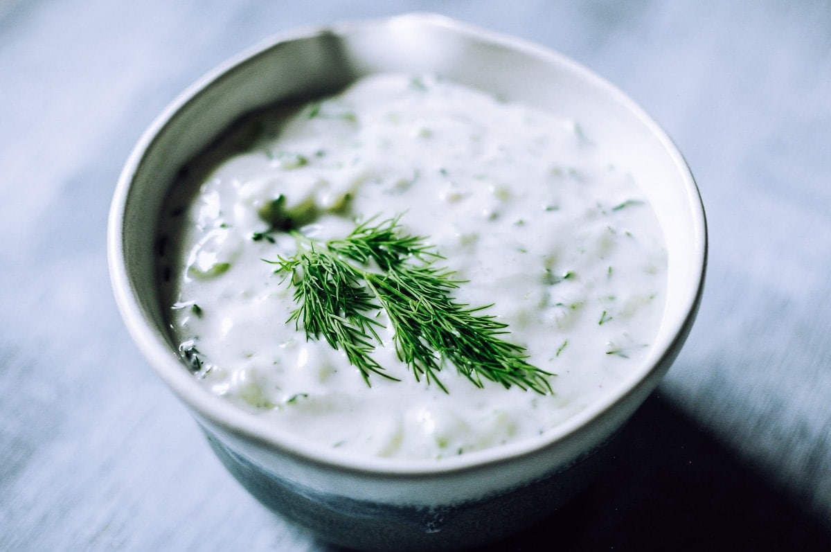 A bowl of creamy white, gluten-free dip garnished with fresh dill on top, set on a light-colored surface—a perfect addition to your collection of gluten-free sauces.