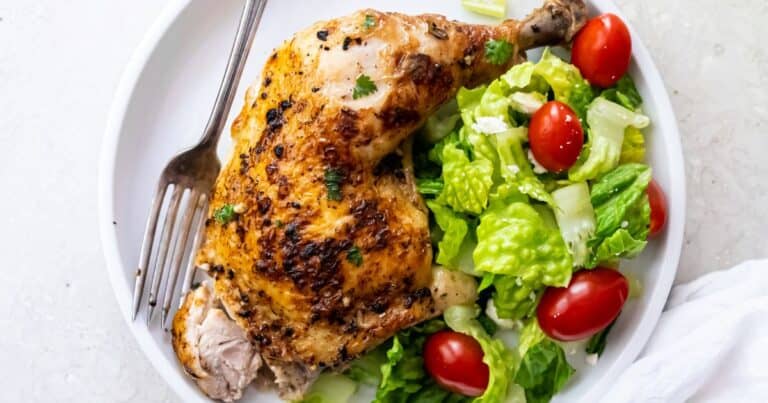 A plate with a roasted chicken leg quarter and a fresh salad of romaine lettuce and grape tomatoes, served with a fork on the side—perfect for those seeking low carb dinners.