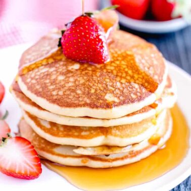A stack of pancakes topped with a whole strawberry and syrup, served on a white plate with sliced strawberries on the side—perfect for a flavorful breakfast.