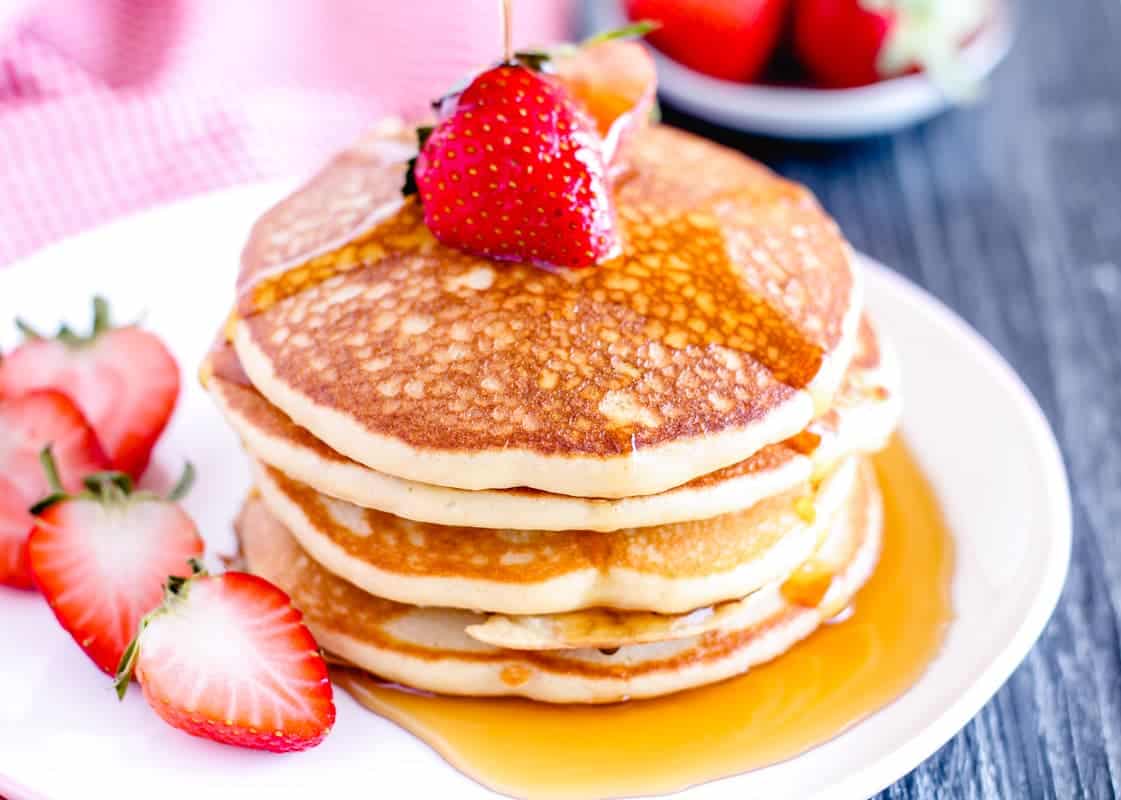 A stack of pancakes topped with a whole strawberry and syrup, served on a white plate with sliced strawberries on the side—perfect for a flavorful breakfast.
