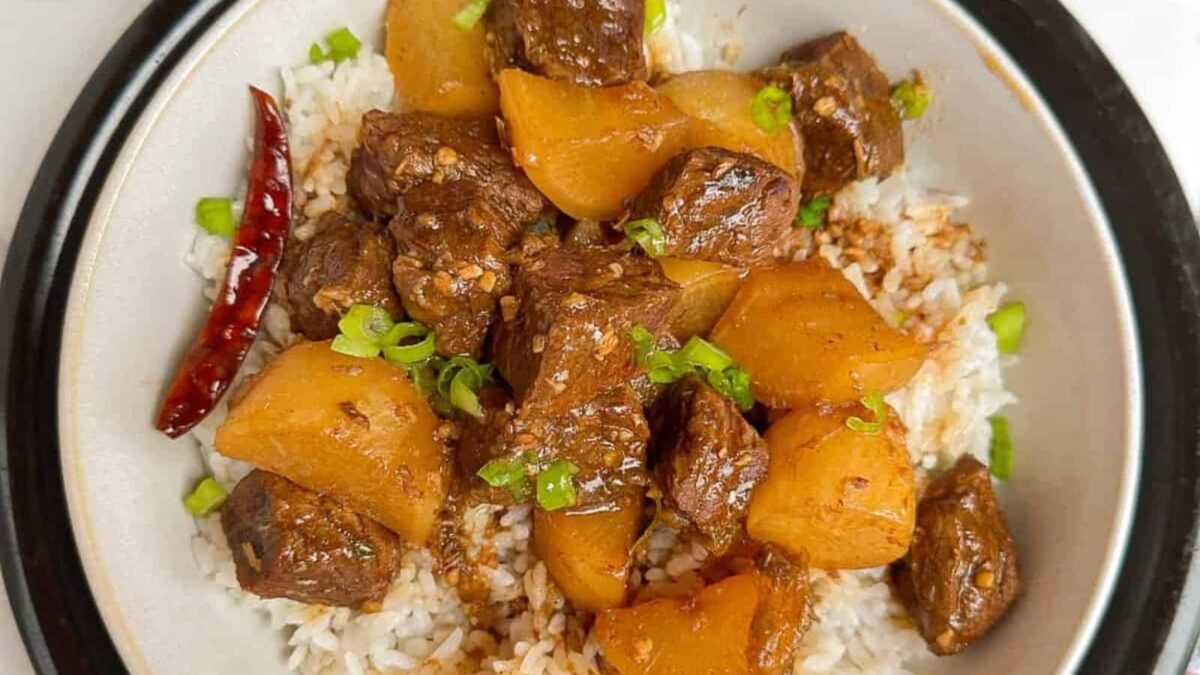 A bowl of white rice topped with chunks of stewed beef, potatoes, a dried red chili, and garnished with chopped green onions—a classic comfort food inspired by homestyle stew recipes.