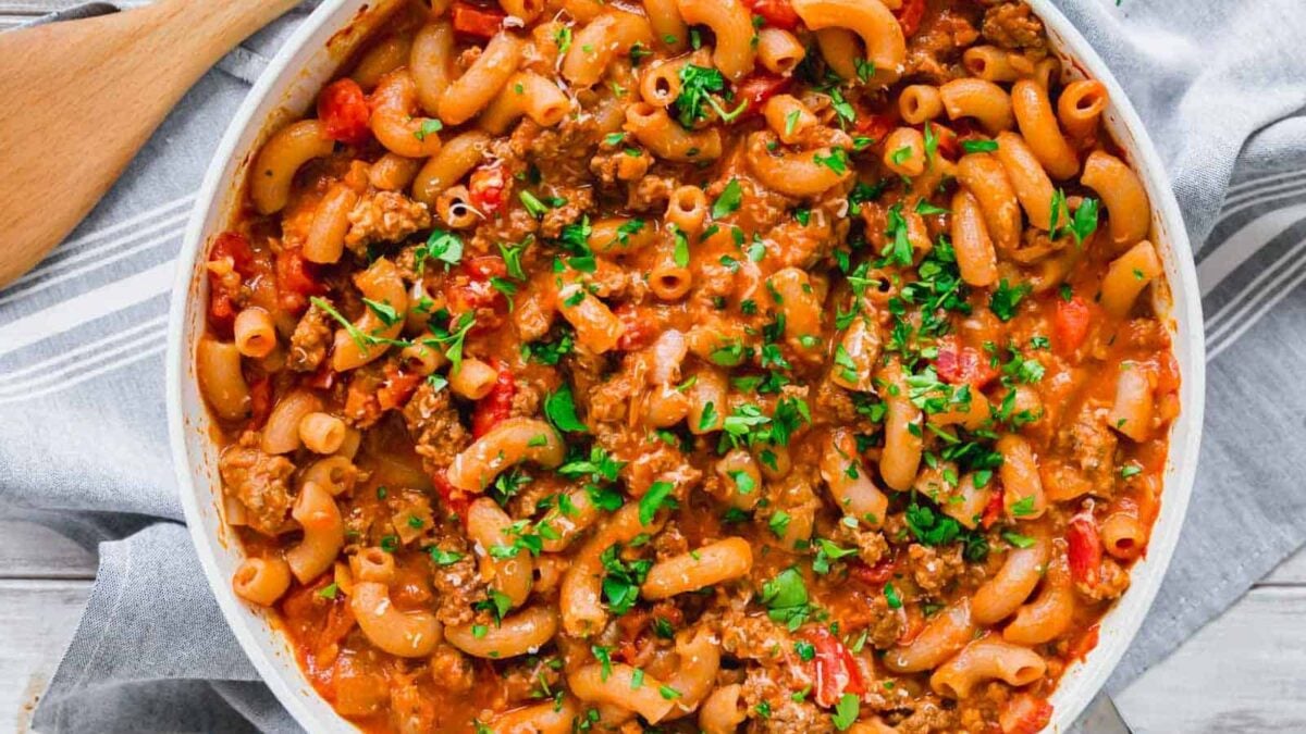 A skillet filled with cooked elbow macaroni, ground beef, tomatoes, and sauce, garnished with chopped parsley—a classic choice for satisfying meals and an easy addition to your collection of ground beef recipes.