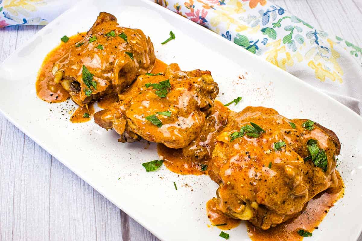 Three pieces of Instant Pot chicken covered in a rich orange sauce and garnished with chopped herbs are arranged on a rectangular white plate—perfect for quick, flavorful chicken dinners.