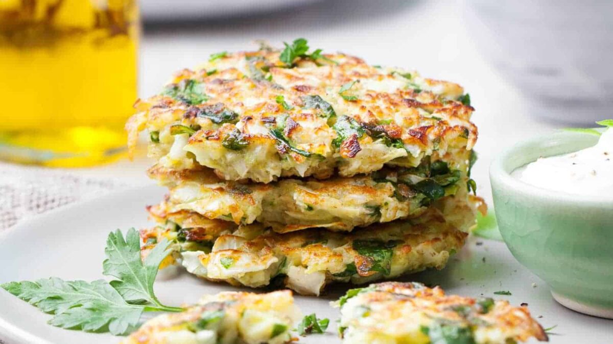 A stack of three golden fritters garnished with fresh herbs, served on a plate with a dollop of white dipping sauce on the side—perfect inspiration for flavorful fritter recipes.