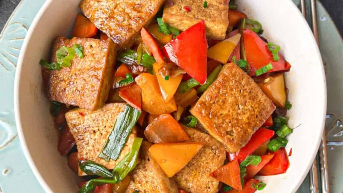 A bowl of stir-fried tofu cubes with sliced red bell peppers, carrots, and green onions, served on a light-colored plate—perfect for everyday cooking and those seeking delicious egg-free recipes.