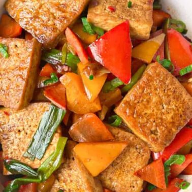 A bowl of stir-fried tofu cubes with sliced red bell peppers, carrots, and green onions, served on a light-colored plateโperfect for everyday cooking and those seeking delicious egg-free recipes.