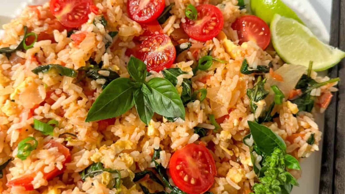 A plate of fried rice garnished with halved cherry tomatoes, fresh basil leaves, chopped green onions, and lime wedges—perfect as one of your light mains or served alongside other fresh sides for spring dishes.