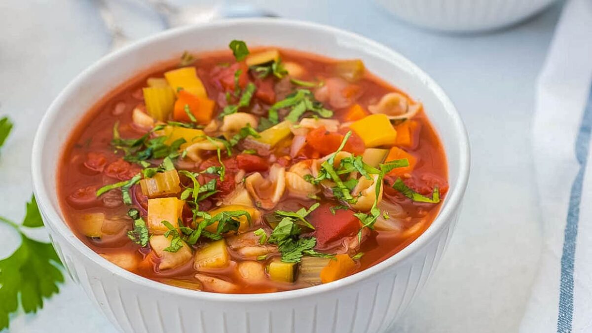 A white bowl filled with vegetable soup containing diced tomatoes, carrots, celery, pasta, and fresh herbs on top—one of those easy soup recipes perfect for enjoying a comforting flavor any day.