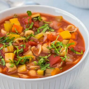 A white bowl filled with vegetable soup containing diced tomatoes, carrots, celery, pasta, and fresh herbs on top—one of those easy soup recipes perfect for enjoying a comforting flavor any day.