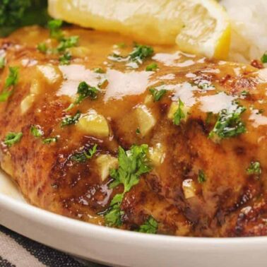 A plate with a piece of chicken breast covered in a lemon herb sauce, served with white rice, broccoli, and lemon wedges—one of those satisfying meals perfect for quick dinner recipes.