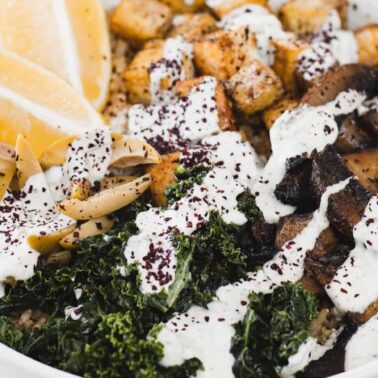 A bowl of rice topped with kale, roasted tofu for silky protein, mushrooms, artichoke hearts, lemon wedges, and a drizzle of white sauce makes for a flavorful twist on classic tofu recipes.