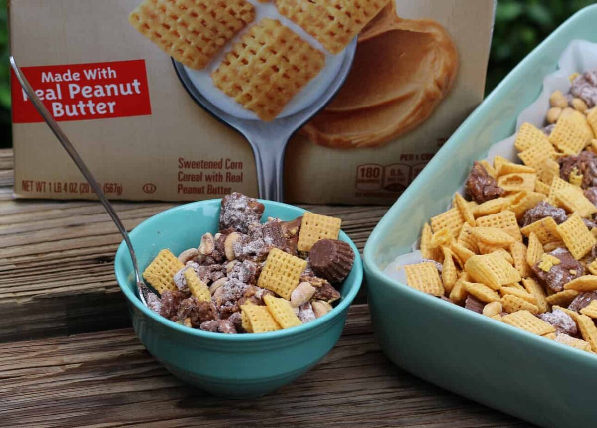 A bowl and a baking dish filled with cereal, chocolate pieces, and peanut butter cups make perfect craving snacks, with a cereal box labeled "Made with Real Peanut Butter" in the background.