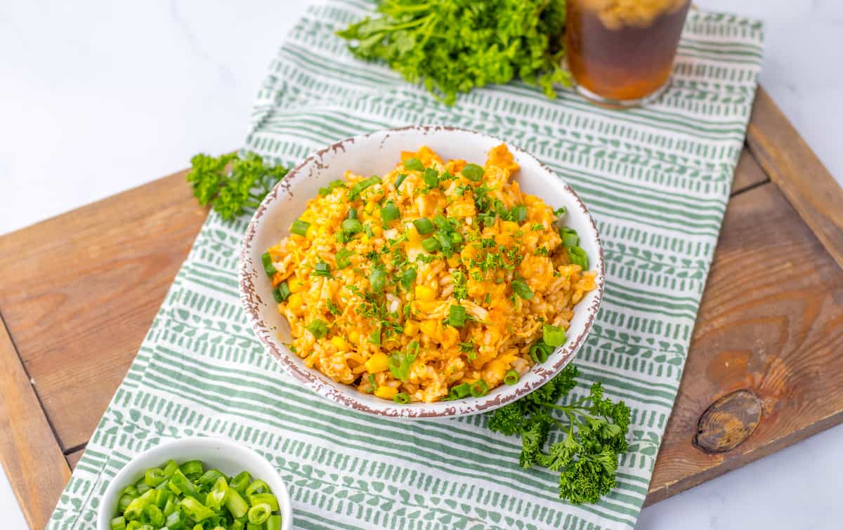 A savory protein bowl of scrambled eggs topped with chopped green onions and parsley sits on a striped cloth, with a small bowl of green onions and fresh herbs nearby.