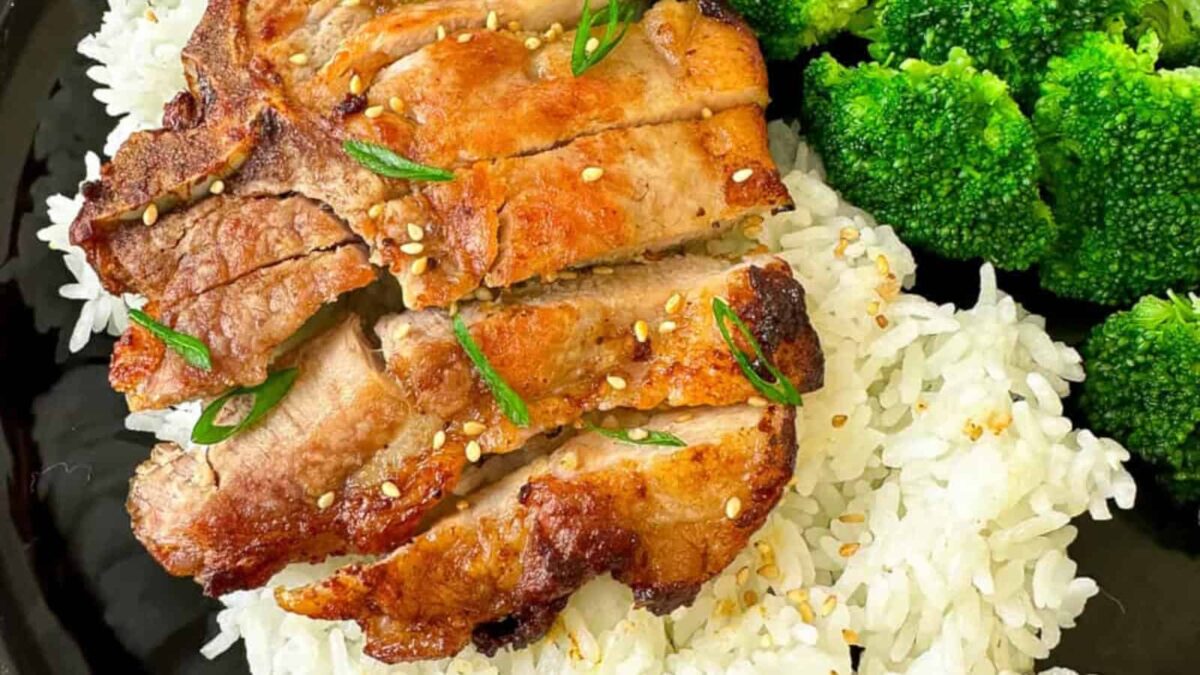 Grilled sliced pork served over white rice, garnished with sesame seeds and green onions, with steamed broccoli on the side— a high-protein meal bursting with fresh flavor.
