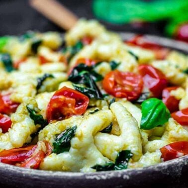A bowl of pasta topped with wilted spinach, cherry tomatoes, and fresh basil leaves, capturing the fresh flavors of spring recipes and served in a rustic wooden bowl.