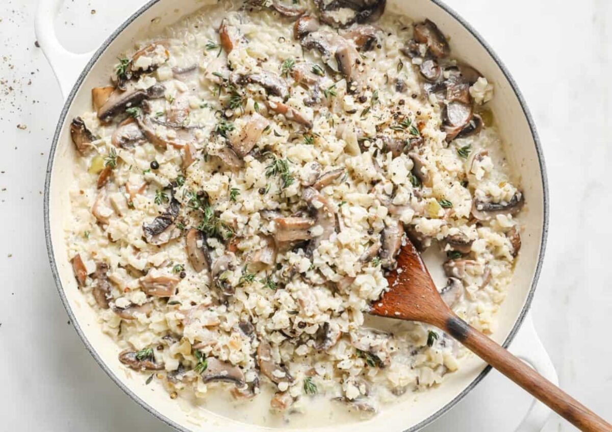 A creamy mushroom risotto in a white pan, rich in flavor and mixed with herbs, is stirred with a wooden spoon, creating a dish full of tempting aroma and color.