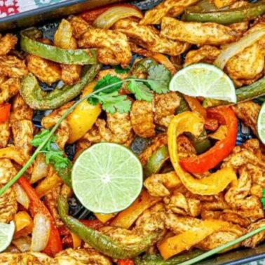 A tray of air fryer chicken fajitas with crispy skin, served with sliced bell peppers, onions, lime wedges, and a cilantro garnish.