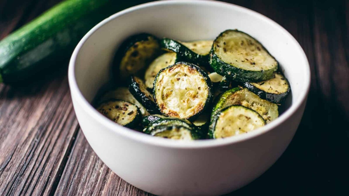 A white bowl filled with sliced, roasted zucchini, perfect for serving as crispy appetizers or new air fryer appetizer ideas, placed on a wooden surface.
