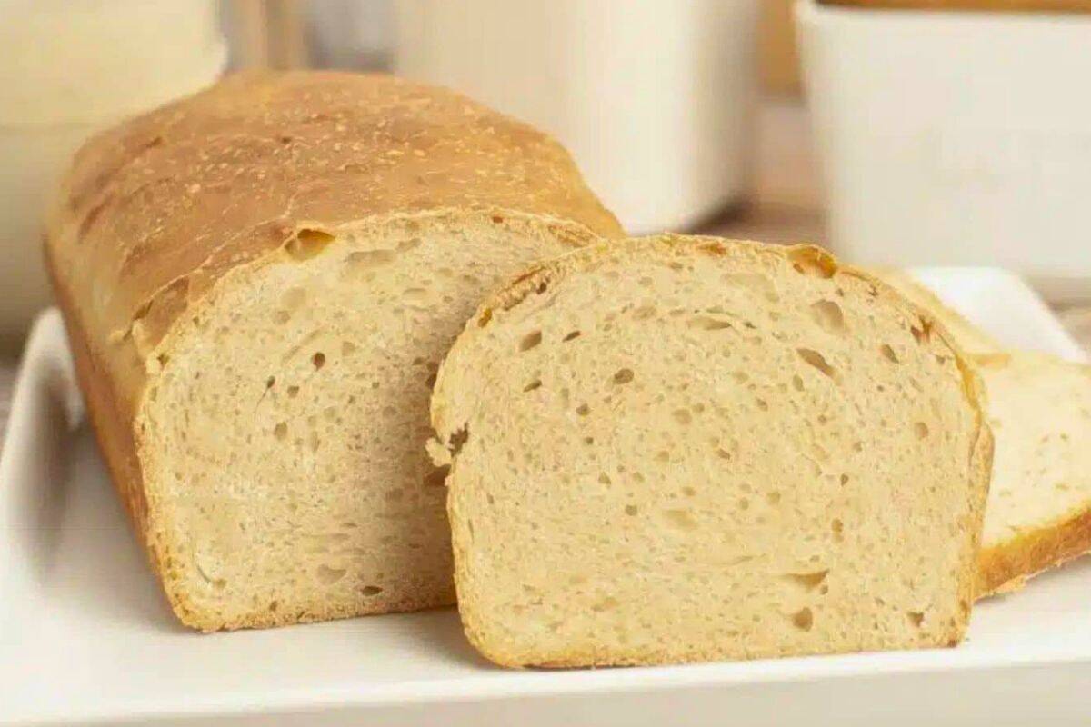 A loaf of plain white bread with two slices cut, displayed on a white rectangular plate in a cozy kitchen setting.