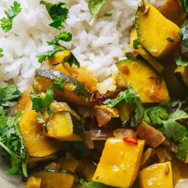 A plate with white rice and flavorful vegetable curry garnished with fresh cilantro.