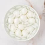 A bowl filled with peeled hard-boiled eggs and ice cubes sits on a marble surface.