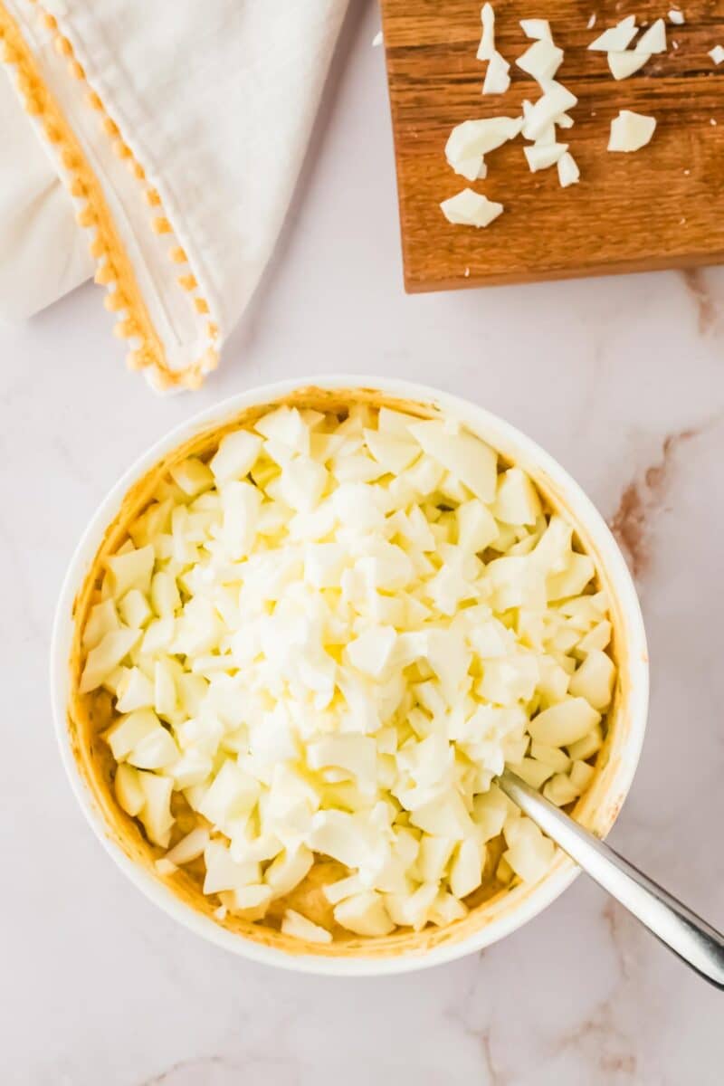 A bowl of chopped hard-boiled eggs with a spoon, next to a cutting board with more chopped eggs and a white cloth on a marble surface.