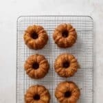 Six mini Bundt cakes are arranged in two rows on a wire cooling rack set on a light-colored surface.