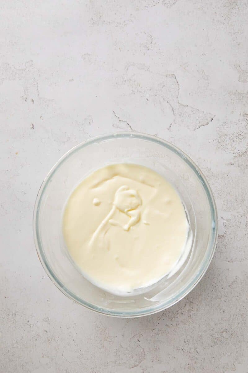 A glass bowl containing a thick, pale cream mixture sits on a light textured surface.