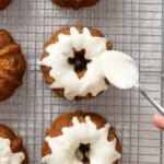 A hand uses a spoon to drizzle white icing onto mini bundt cakes arranged on a wire cooling rack.