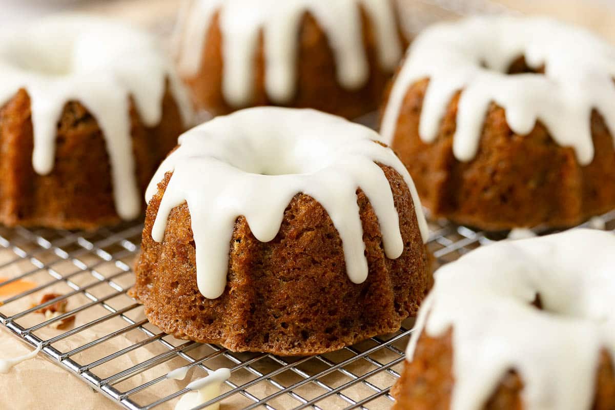 Mini bundt cakes with white icing drizzle sit on a cooling rack.