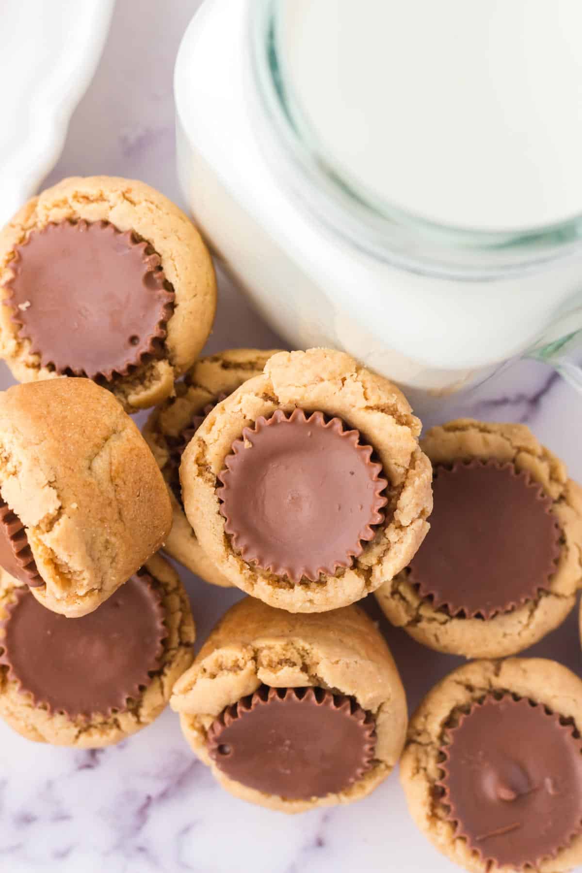 Peanut butter cookies with chocolate centers arranged next to a glass of milk on a marble surface.