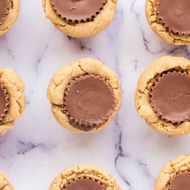 Peanut butter cookies topped with chocolate peanut butter cups arranged on a white marble surface.