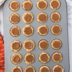 A muffin tin filled with 24 peanut butter cup cookies, each topped with a chocolate peanut butter cup, on a marble countertop.