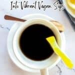 A cup of black coffee with a lemon twist on the rim sits on a white saucer, with a wooden spoon, next to a plate of lemon slices on a marble surface. Text overlay present.