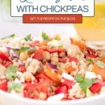 A bowl of quinoa salad with chickpeas, red bell pepper, red onion, cilantro, and feta cheese, with a citrus dressing being poured on top. Text overlay promotes the recipe on a blog.