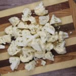 Chopped cauliflower florets spread out on a striped wooden cutting board.