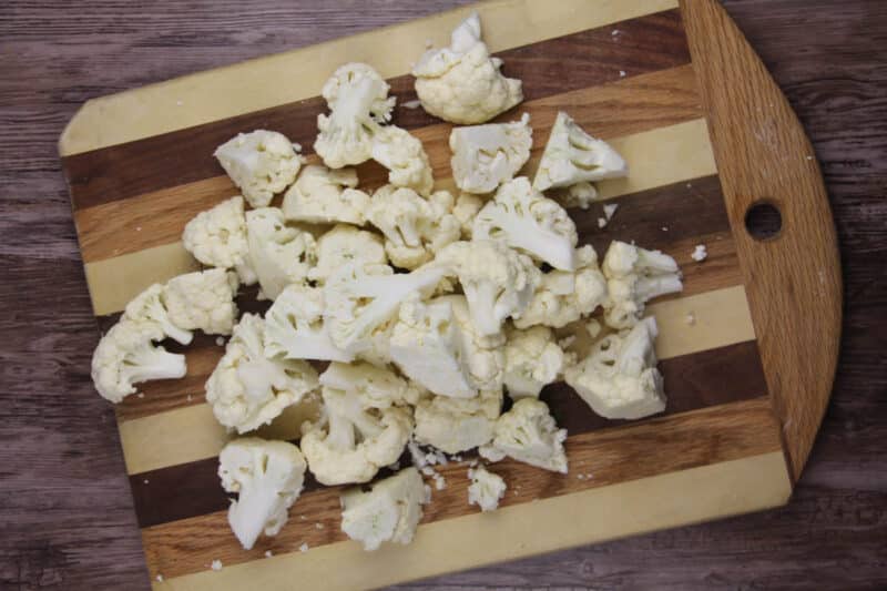 Chopped cauliflower florets spread out on a striped wooden cutting board.