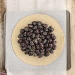 A round sheet of dough on parchment paper topped with sugared blackberries, placed on a baking tray over a wooden surface.