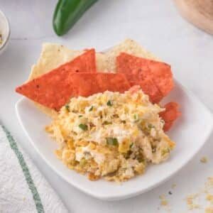 A plate with a serving of creamy dip mixed with green onions, accompanied by red and white tortilla chips.