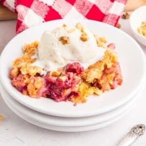 A serving of cherry pineapple dump cake topped with a scoop of vanilla ice cream and sprinkled with chopped nuts, on a white plate.