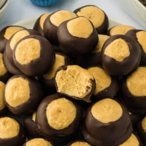 A plate of buckeye candies with chocolate-coated peanut butter balls, one with a bite taken out showing the creamy filling.