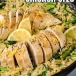 Sliced lemon chicken served over creamy orzo pasta with spinach and asparagus in a skillet, garnished with lemon wedges and zest.