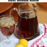 A glass and pitcher of iced tea with ice cubes sit on a table next to two lemons and a red-patterned white cloth.