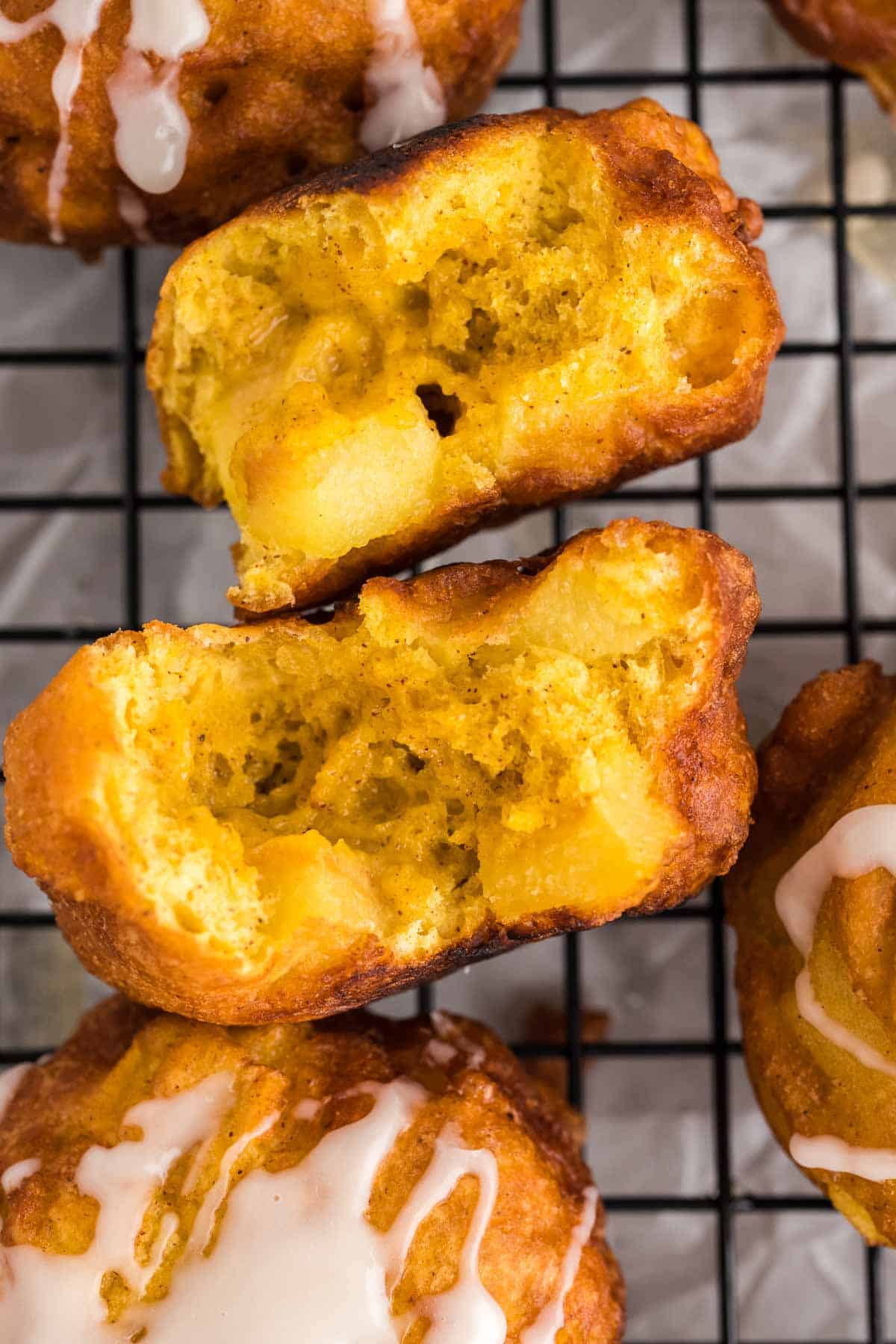 Close-up of sliced apple fritters with a golden, moist interior, resting on a cooling rack with a light glaze drizzled on top.