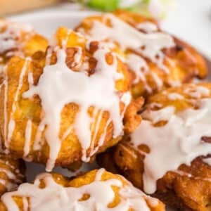 A close-up of several apple fritters topped with white icing, arranged on a plate.