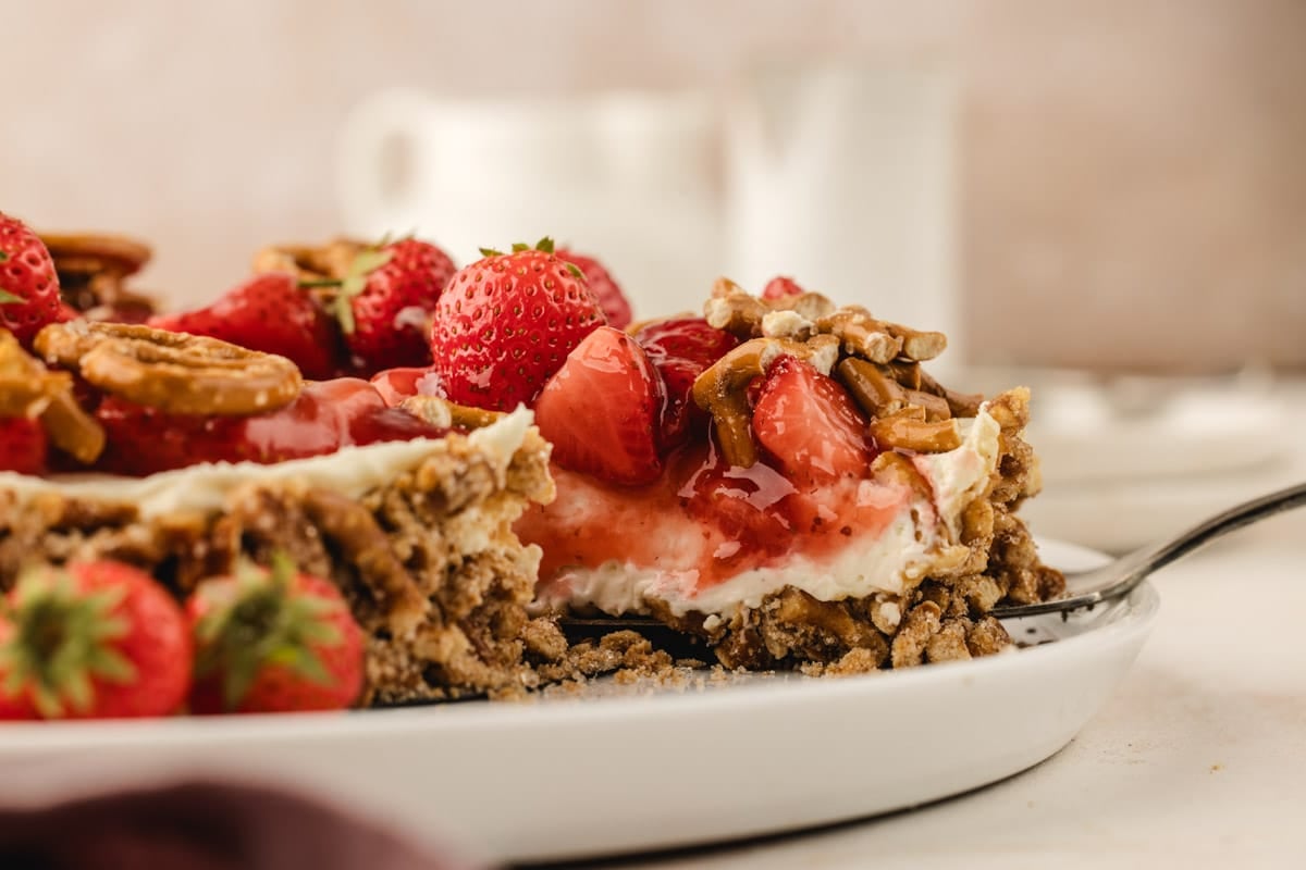 A slice of strawberry pretzel pie on a white plate with a fork.